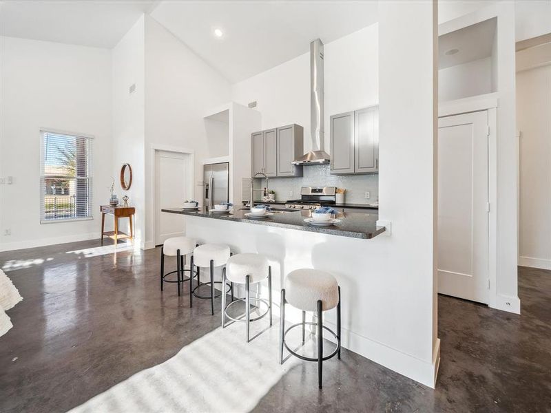 Kitchen with gray cabinets, appliances with stainless steel finishes, a high ceiling, wall chimney range hood, and a breakfast bar