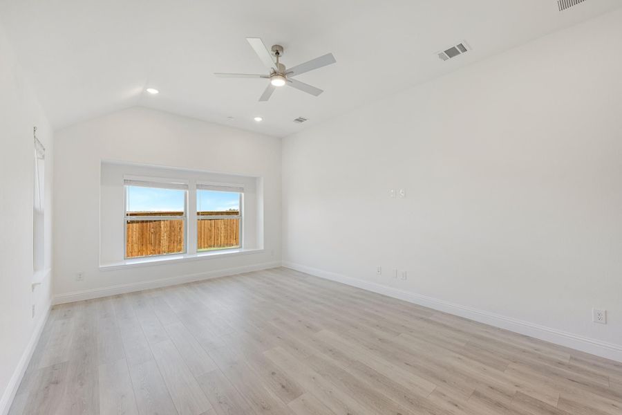 Empty room with vaulted ceiling, ceiling fan, light wood floors, and double window with backyard view Empty room with vaulted ceiling, ceiling fan, light wood floors, and double window with backyard view