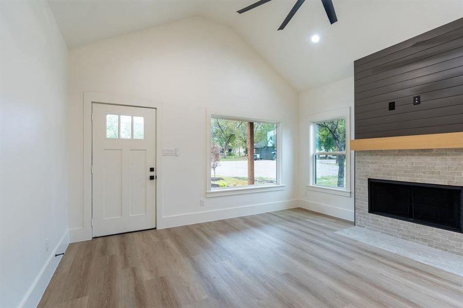 Unfurnished living room featuring light wood-type flooring, a fireplace, ceiling fan, and high vaulted ceiling