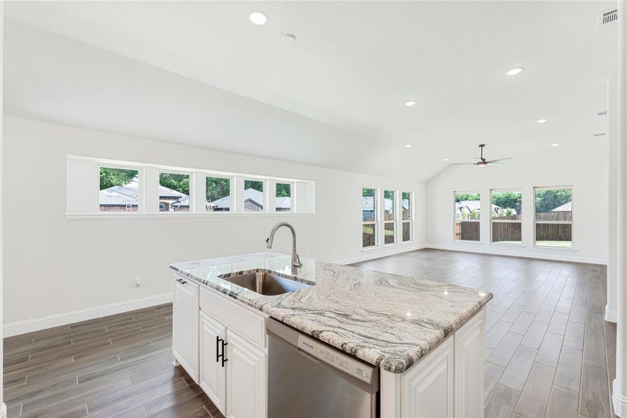 Kitchen island with granite countertop and sink, open to living area with vaulted ceiling and large windows Kitchen island with granite countertop and sink, open to living area with vaulted ceiling and large windows