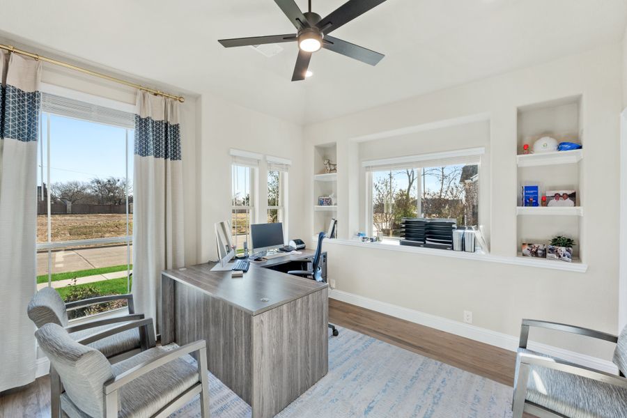 Home office with L-shaped desk, built-in shelves, ceiling fan, and large windows with natural light Home office with L-shaped desk, built-in shelves, ceiling fan, and large windows with natural light