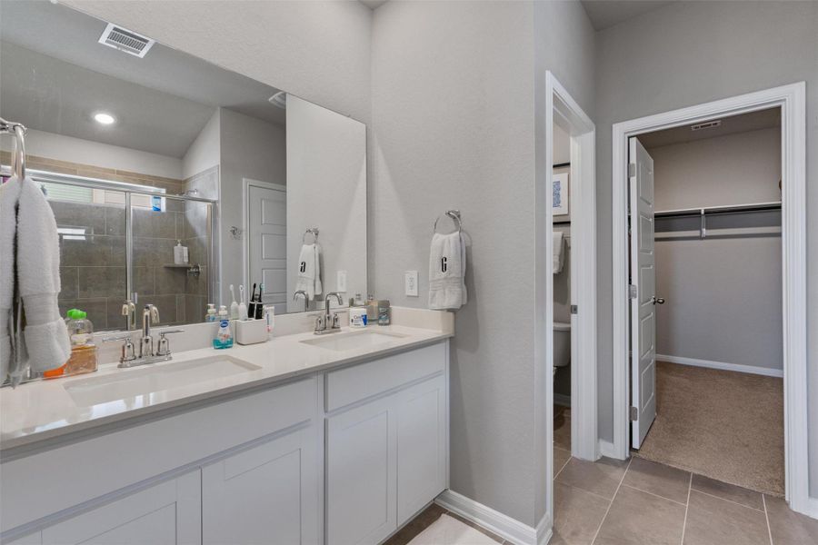 Bathroom featuring a dual vanity with white cabinetry, a large wall-mounted mirror, and a glass-enclosed shower with tiled walls Bathroom featuring a dual vanity with white cabinetry, a large wall-mounted mirror, and a glass-enclosed shower with tiled walls