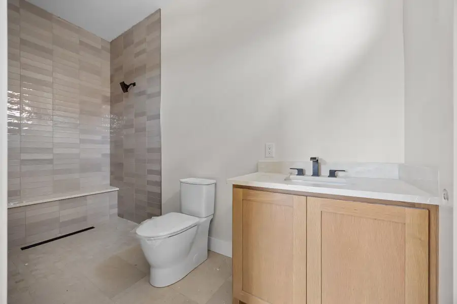 Walk-in shower featuring light-toned rectangular tile, integrated bench seating, and a linear drain