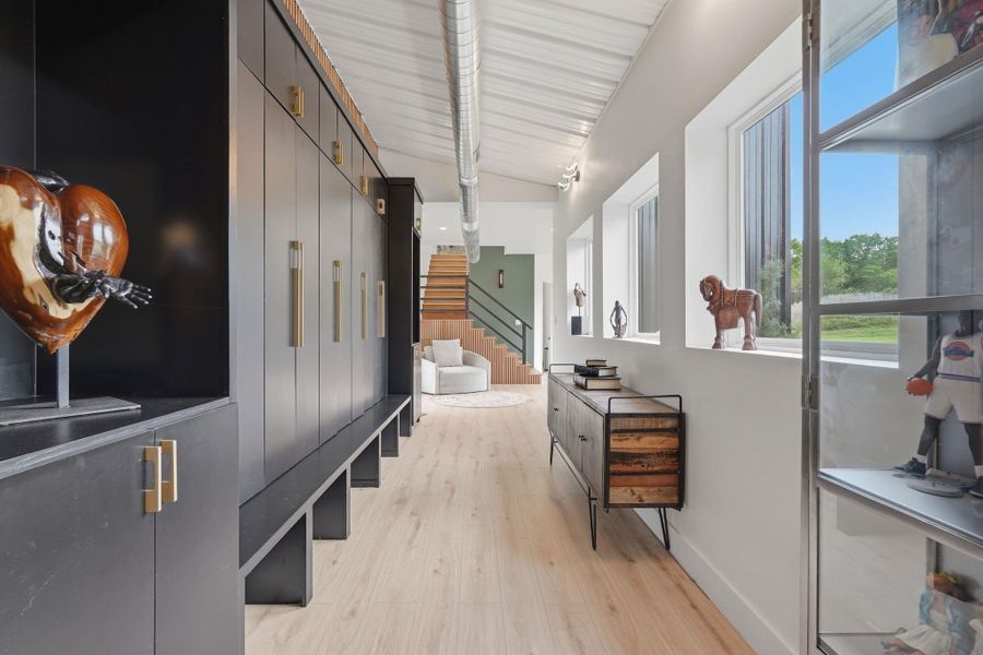 This photo showcases a modern hallway with sleek black cabinetry on one side and large windows on the other, allowing plenty of natural light. The light wood flooring and contemporary decor create an inviting, stylish atmosphere. At the end of the hallway, a staircase leads to the upper level, adding architectural interest.