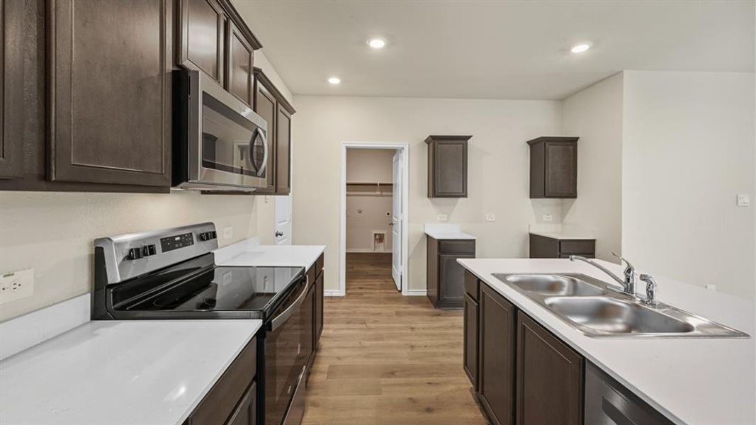 Spacious kitchen featuring dark wood-finish cabinetry, light countertops, wood-finish flooring, a stainless steel double basin sink, and recessed lighting