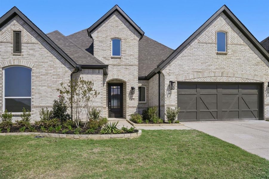 French provincial home featuring brick siding, a front yard, driveway, and a shingled roof