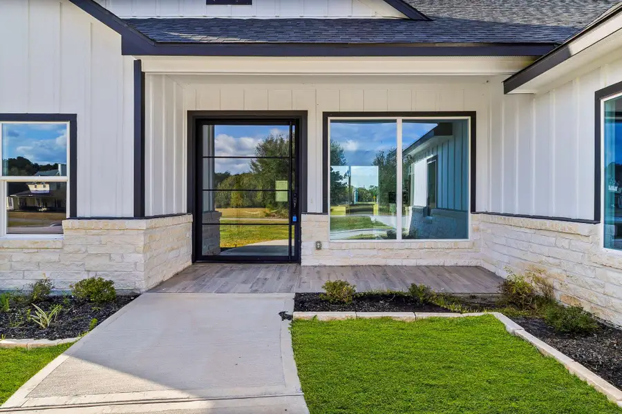 This photo showcases a modern home's inviting entrance with a glass door, large window, and a blend of stone and siding. The pathway and landscaped front yard add to its curb appeal. This photo showcases a modern home's inviting entrance with a glass door, large window, and a blend of stone and siding. The pathway and landscaped front yard add to its curb appeal.
