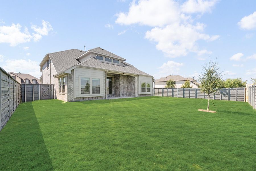 Backyard view of brick and siding home with large green lawn, covered patio, and wood privacy fence Backyard view of brick and siding home with large green lawn, covered patio, and wood privacy fence