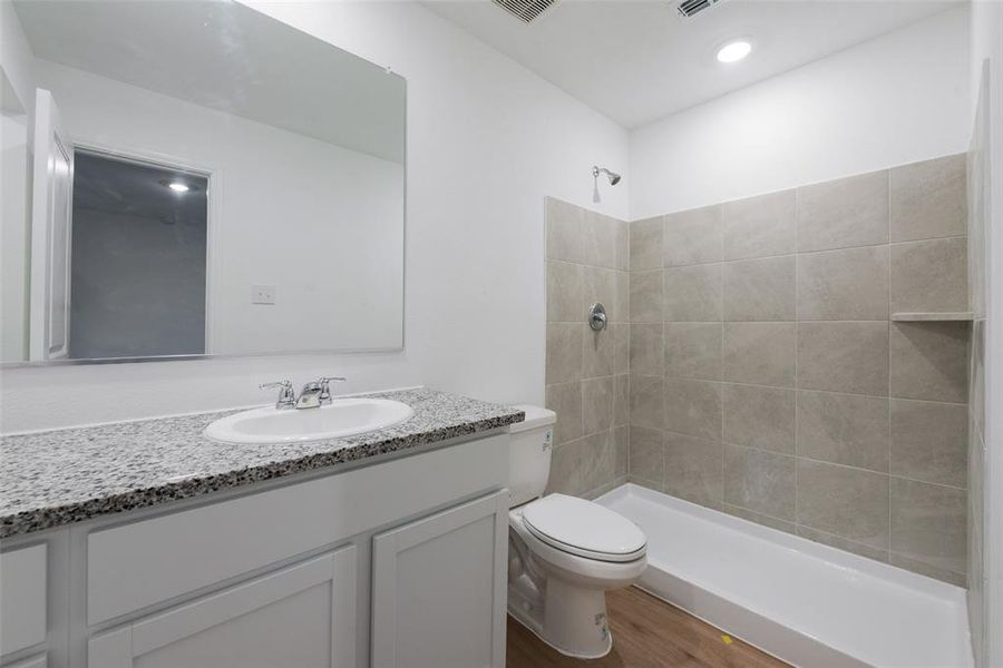 Bathroom featuring a tile shower, vanity, toilet, and wood-type flooring