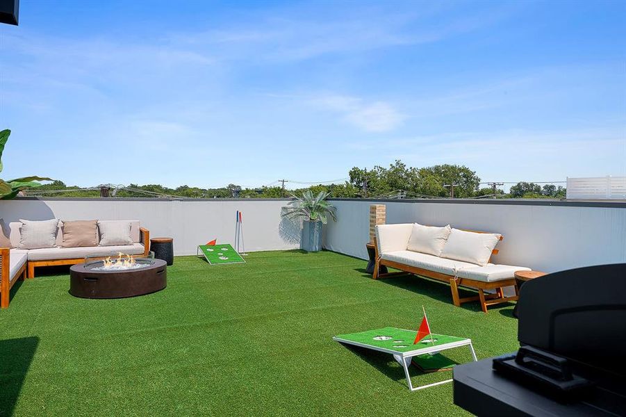 Expansive rooftop deck featuring artificial turf, a built-in fire pit, and white perimeter walls