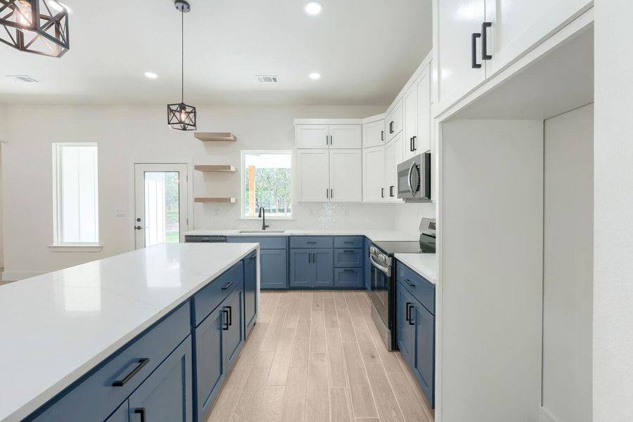 A contemporary kitchen features bright white and deep blue cabinetry, sleek countertops, and modern pendant lighting.