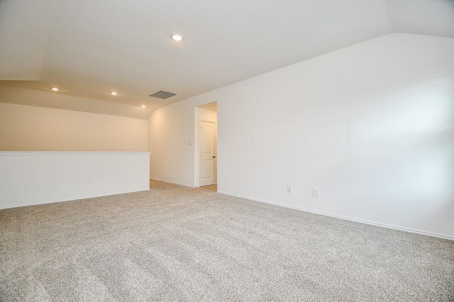 This photo shows a spacious, well-lit room with neutral carpeting, recessed lighting, and clean white walls, ideal for a versatile living area or office space.