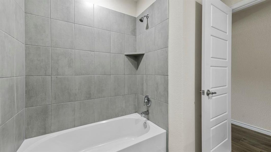 Bathroom featuring a white bathtub with a tile surround, a built-in shower niche, and a showerhead with a separate faucet