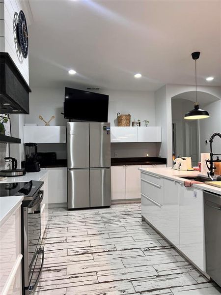 Kitchen featuring sink, premium range hood, white cabinetry, stainless steel appliances, and pendant lighting