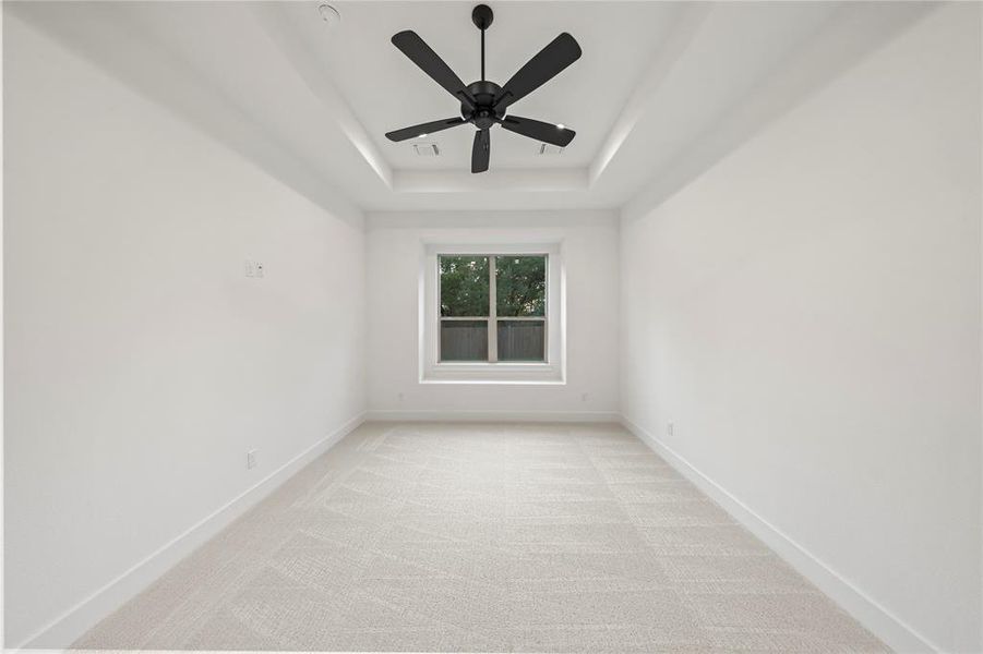 Unfurnished room featuring light carpet, a tray ceiling, and a ceiling fan