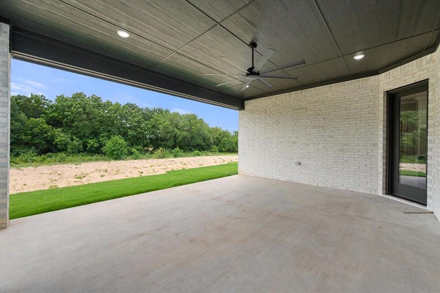Expansive covered patio featuring a concrete surface, white brick wall, and a dark wood-finish ceiling with recessed lighting