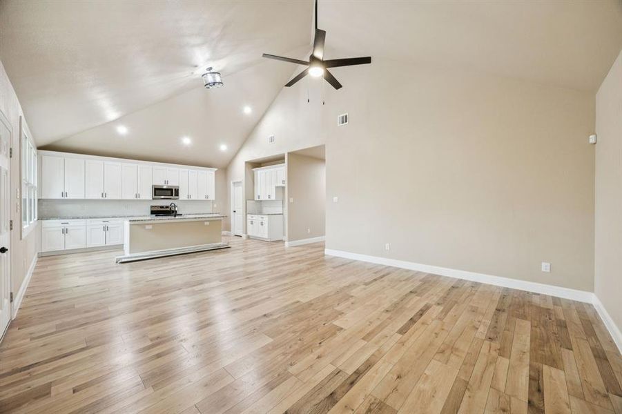 Unfurnished living room featuring high vaulted ceiling, light wood-style floors, and ceiling fan Unfurnished living room featuring high vaulted ceiling, light wood-style floors, and ceiling fan