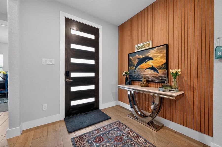 The entryway features light-toned hardwood flooring and a dark wood door with horizontal frosted glass inlays