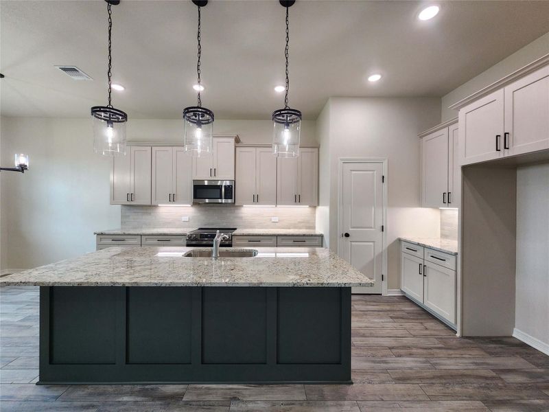 Spacious kitchen featuring a large island with a stone countertop, pendant lighting, built-in stainless steel appliances, light-toned cabinetry, and wood-finish flooring
