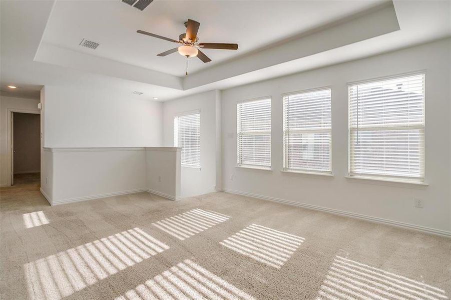 Carpeted empty room featuring a raised ceiling and ceiling fan