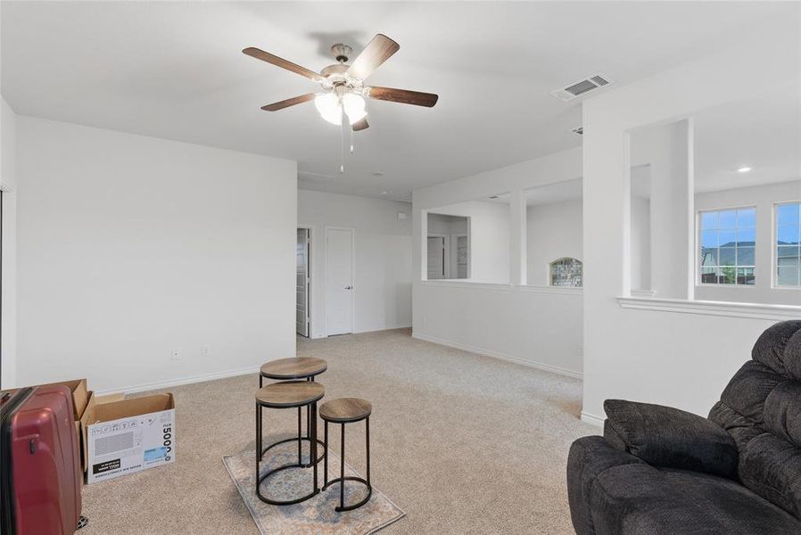 Carpeted upper-level landing featuring a ceiling fan with light fixture, white walls, and a half-wall overlooking a lower level