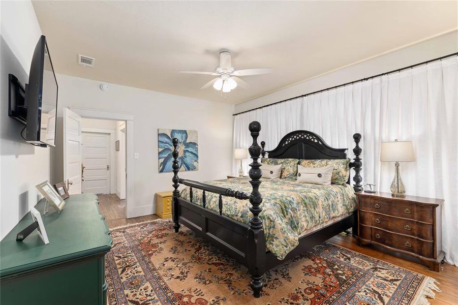 Bedroom featuring wood-finish flooring, a ceiling fan, and white window treatments