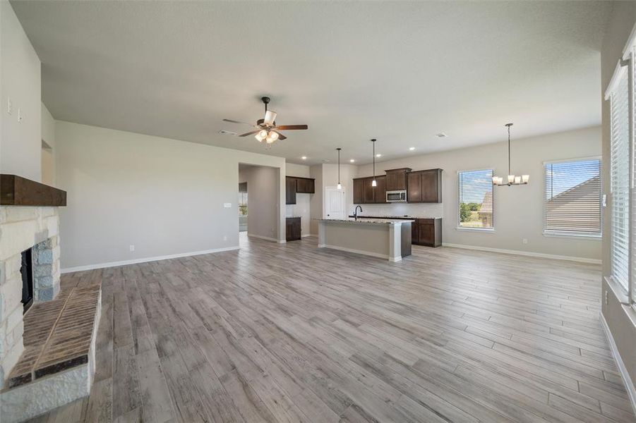 Unfurnished living room with light wood finished floors, recessed lighting, a stone fireplace, a chandelier, and ceiling fan Unfurnished living room with light wood finished floors, recessed lighting, a stone fireplace, a chandelier, and ceiling fan