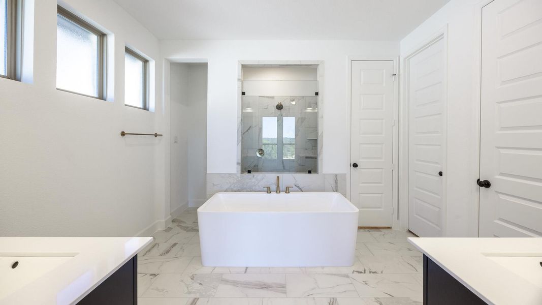 Full bathroom with a freestanding tub, a marble finish shower, two vanities, and light marble finish floors