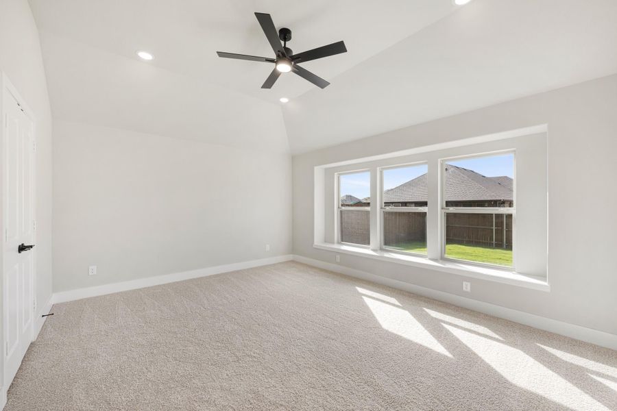 Empty bedroom with vaulted ceiling, black ceiling fan, carpet flooring, and triple windows overlooking backyard