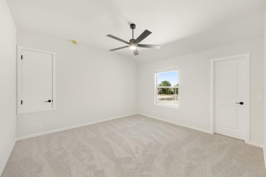Empty bedroom with gray carpet, white walls, ceiling fan, and two doors