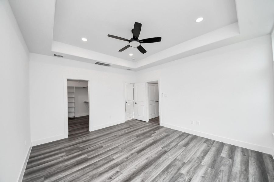This spacious room features sleek vinyl flooring, a modern ceiling fan, recessed lighting, and a tray ceiling. It includes a doorway leading to a closet with built-in shelving, perfect for storage. This spacious room features sleek vinyl flooring, a modern ceiling fan, recessed lighting, and a tray ceiling. It includes a doorway leading to a closet with built-in shelving, perfect for storage.