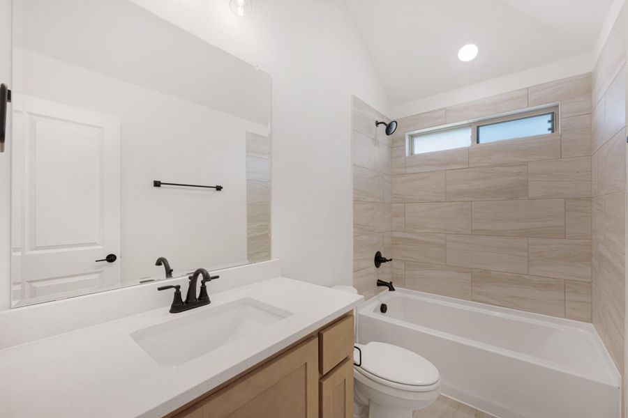 Bathroom with wood vanity, white quartz countertop, and tiled tub-shower combo with small window