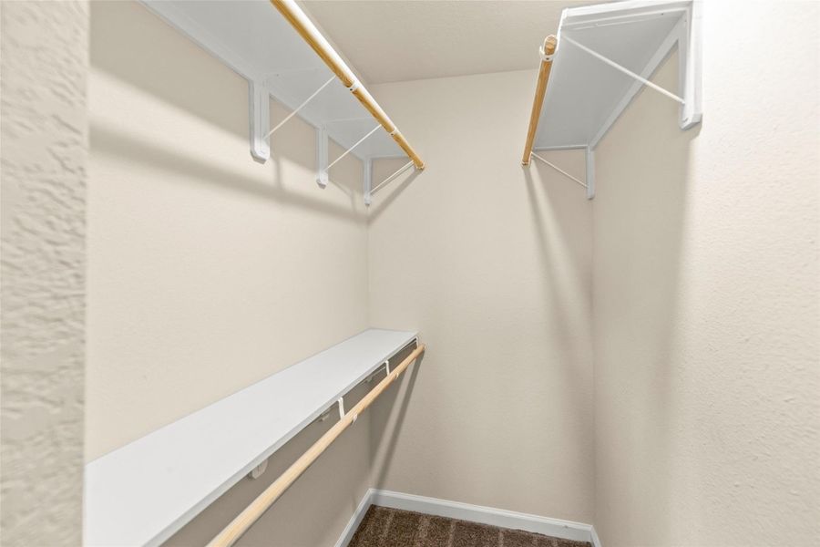 This photo showcases a walk-in closet with ample shelving and hanging space, featuring neutral walls and carpeting. Ideal for organized storage. This photo showcases a walk-in closet with ample shelving and hanging space, featuring neutral walls and carpeting. Ideal for organized storage.