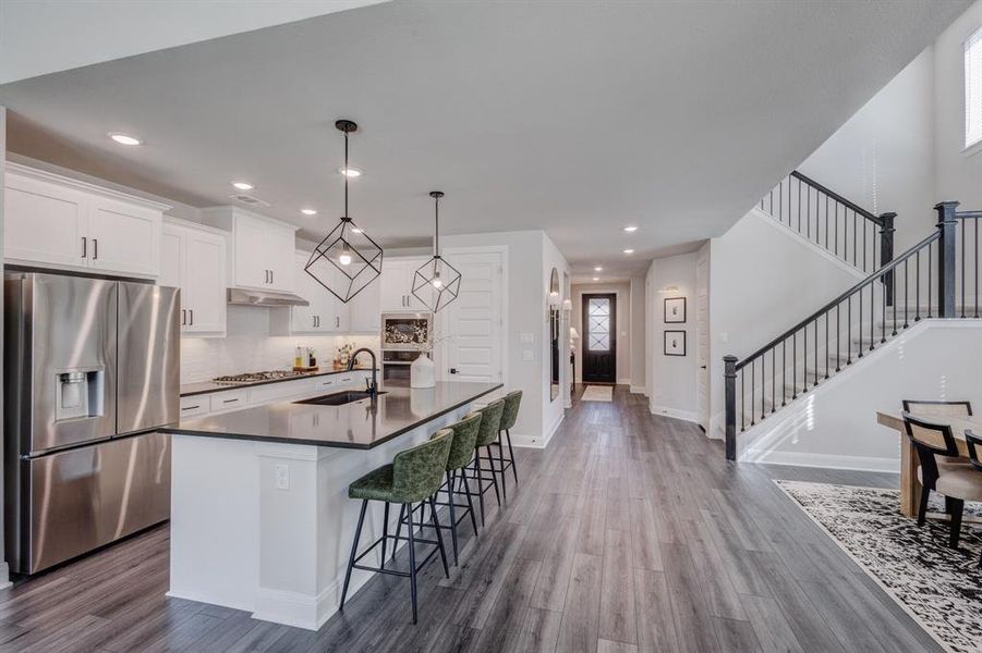 Kitchen featuring appliances with stainless steel finishes, white cabinetry, a center island with sink, hanging light fixtures, and dark wood-style floors