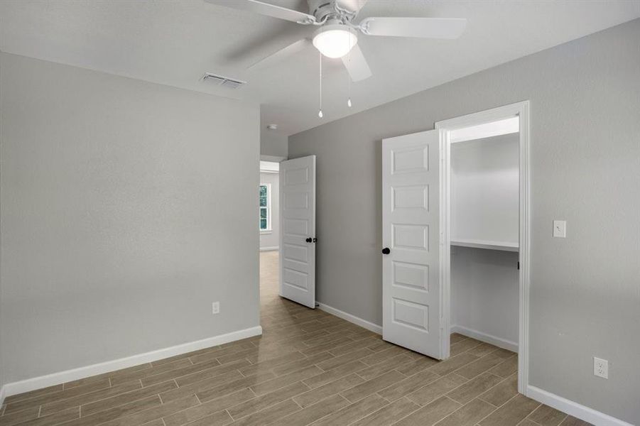 Unfurnished bedroom with a walk in closet, wood tiled floors, and ceiling fan Unfurnished bedroom with a walk in closet, wood tiled floors, and ceiling fan