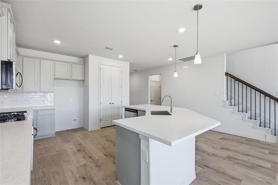 Open-concept kitchen featuring an island with an undermount sink, quartz countertops, light-finish cabinetry, and wood-finish flooring