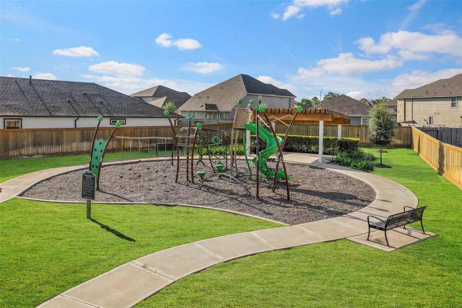 Charming community playground featuring modern play structures, lush green lawns, and a cozy seating area under a pergola, perfect for family fun and relaxation.