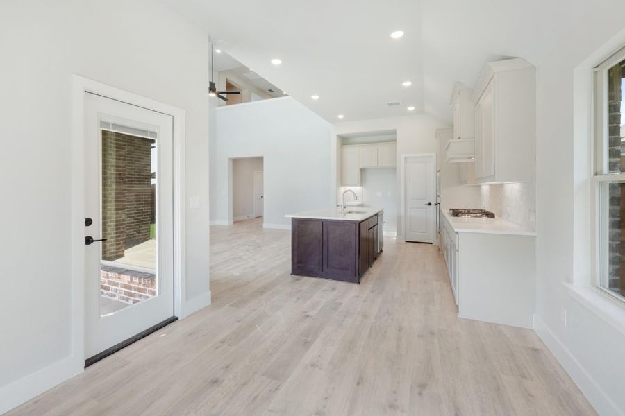 Open kitchen with white cabinets, dark wood island, light hardwood floors, and back door access