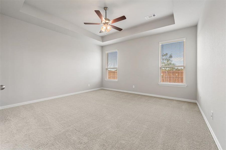 Empty room featuring a raised ceiling, light colored carpet, and a ceiling fan Empty room featuring a raised ceiling, light colored carpet, and a ceiling fan