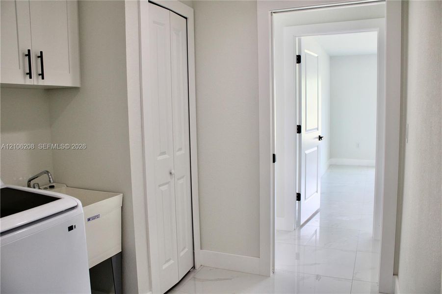 Utility space featuring white shaker-style wall cabinetry with matte black hardware, a basin sink, bifold door storage, and polished stone-finish floor tile