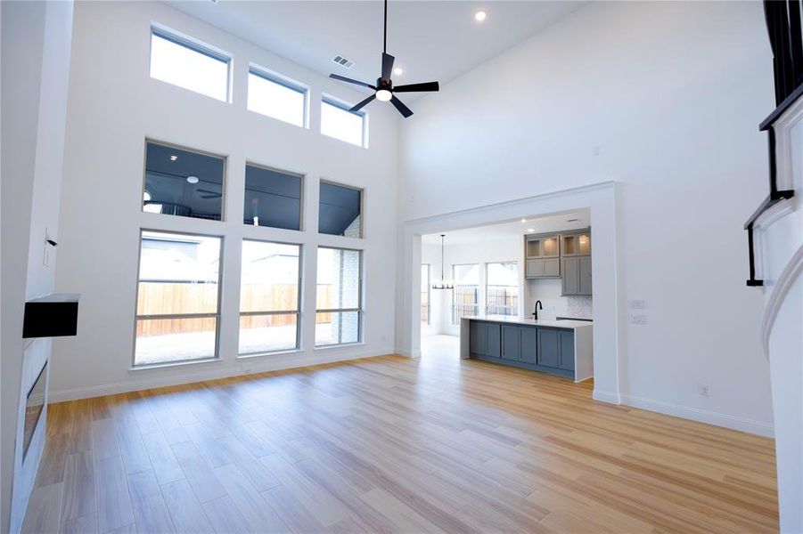 Unfurnished living room with a ceiling fan, light wood-style flooring, a high ceiling, a chandelier, and recessed lighting Unfurnished living room with a ceiling fan, light wood-style flooring, a high ceiling, a chandelier, and recessed lighting