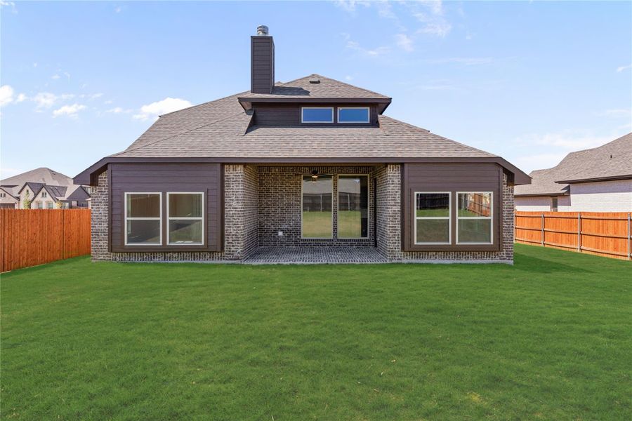 Rear exterior of single-story home with brick and dark siding, covered patio, chimney, and fenced green backyard Rear exterior of single-story home with brick and dark siding, covered patio, chimney, and fenced green backyard