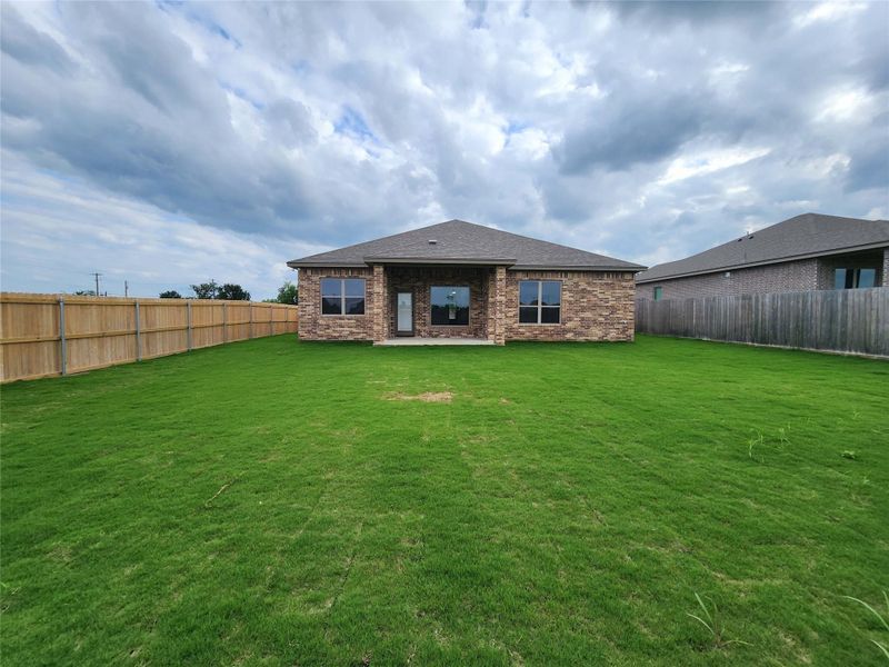 Expansive backyard featuring a manicured lawn, full privacy fencing, and a covered patio area