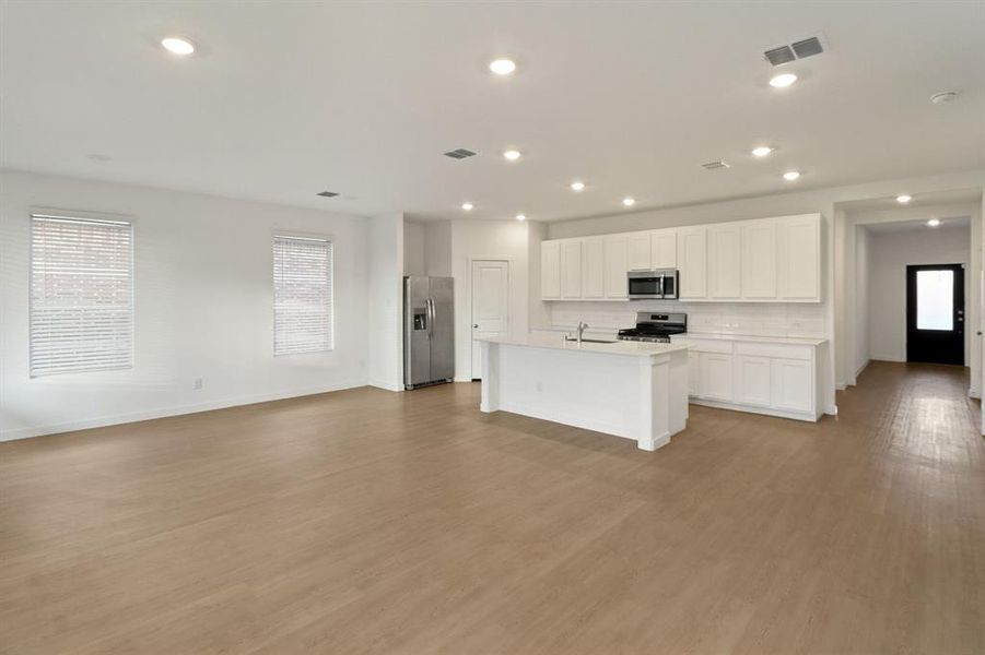 Kitchen featuring stainless steel appliances, white cabinetry, open floor plan, a kitchen island with sink, and light wood-style floors