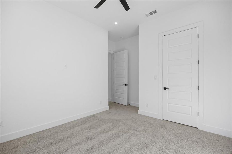 Spacious Kids room featuring light gray carpet, crisp white walls, contemporary white five-panel doors with matte black hardware, and a ceiling fan with integrated lighting
