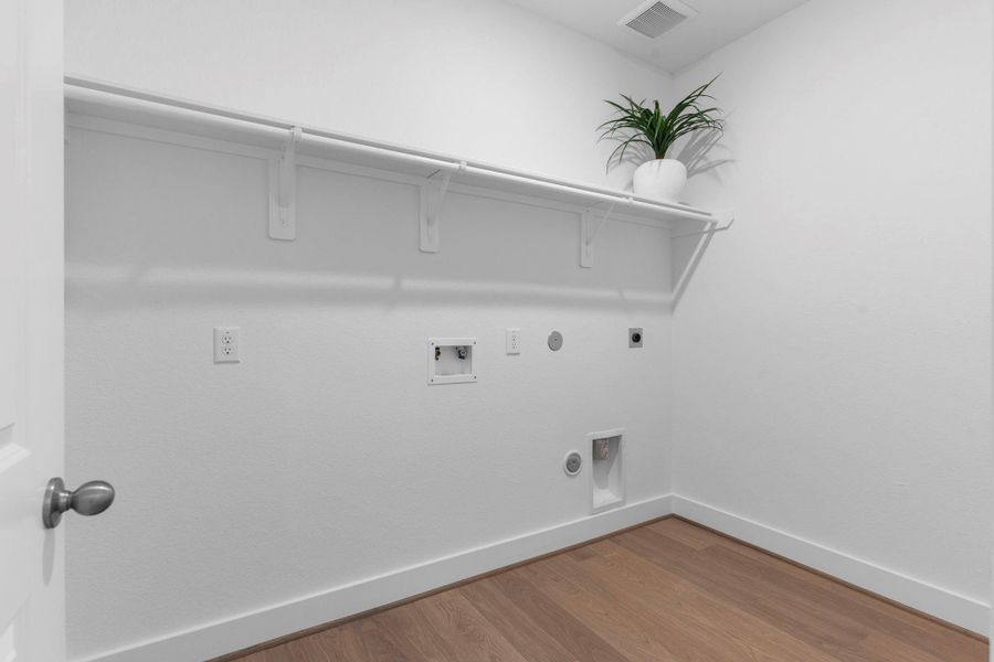 Spacious utility room with upper shelving and woodlike vinyl flooring provides a practical and organized space for laundry day—complete with washer and dryer connections and ample wall space for customization. **Image Representative of Plan Only and May Vary as Built**. Spacious utility room with upper shelving and woodlike vinyl flooring provides a practical and organized space for laundry day—complete with washer and dryer connections and ample wall space for customization. **Image Representative of Plan Only and May Vary as Built**.