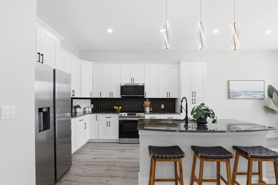 Modern kitchen featuring white cabinetry with black hardware, stainless steel appliances, dark tile backsplash, and a large island with a stone countertop