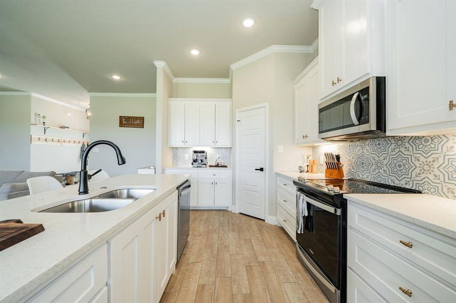 Kitchen with stainless steel appliances, ornamental molding, white cabinets, light wood-style floors, and backsplash Kitchen with stainless steel appliances, ornamental molding, white cabinets, light wood-style floors, and backsplash
