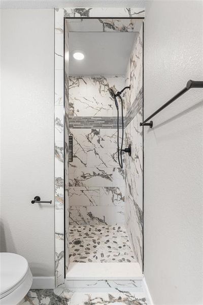 Primary bathroom featuring a shower stall, light marble finish floors, and a textured wall