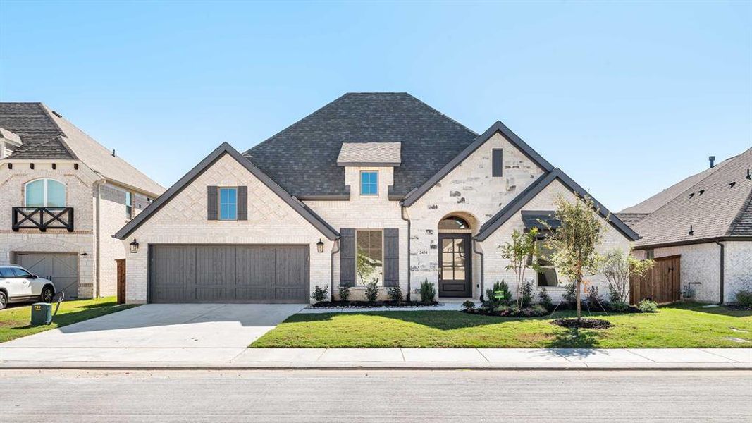 French country inspired facade featuring a garage and a front lawn